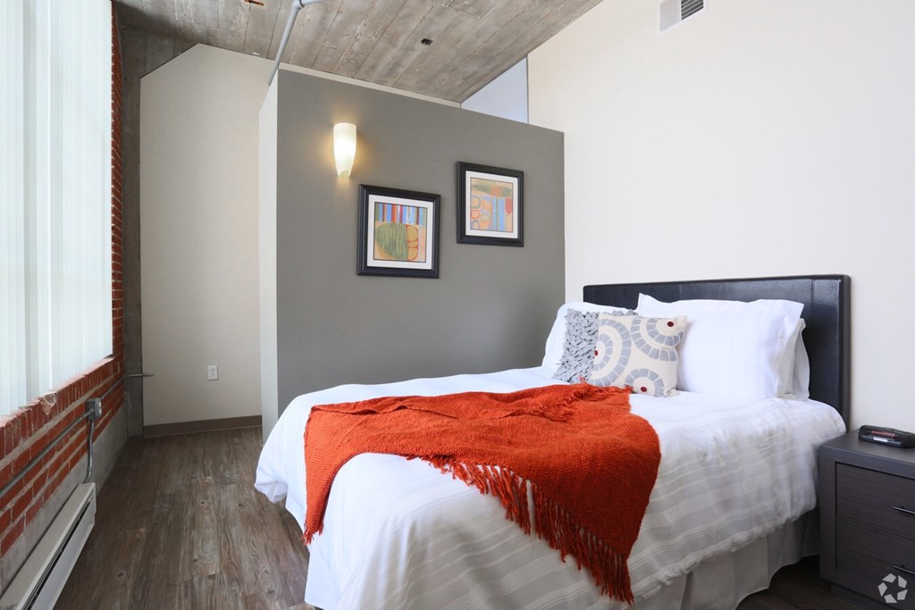 A bedroom with a bed covered in a white comforter and a red throw.