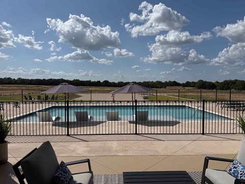 A pool surrounded by a black fence with two umbrellas and chairs.
