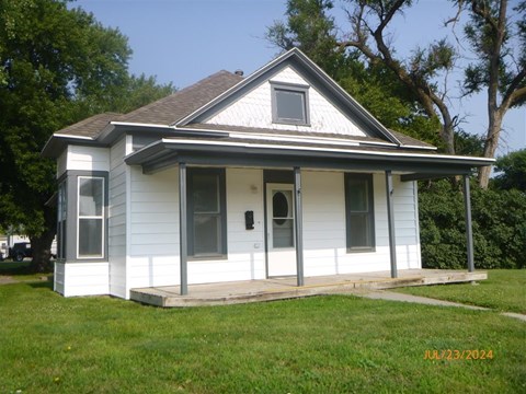 A small white house with a grey roof and a porch.