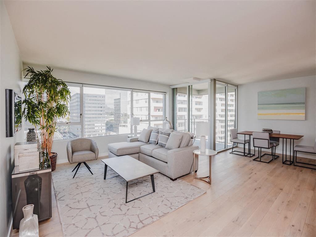 A living room with a grey sofa, a white coffee table, and a large window with a view of the city.