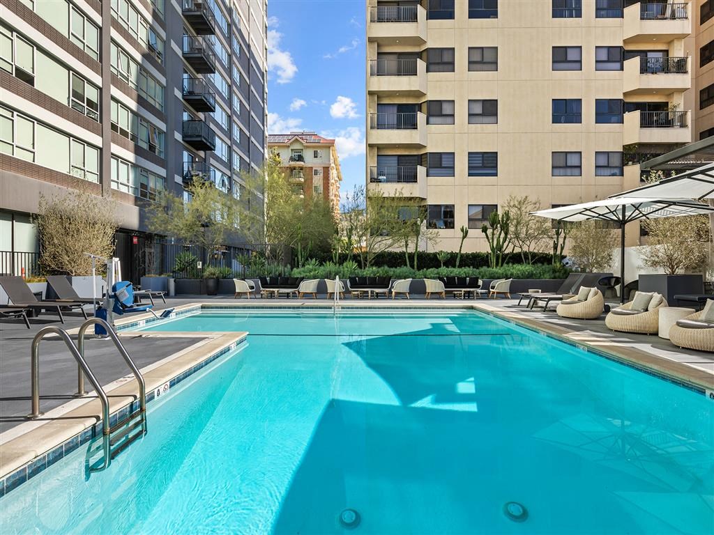 A swimming pool in a hotel surrounded by chairs and umbrellas.