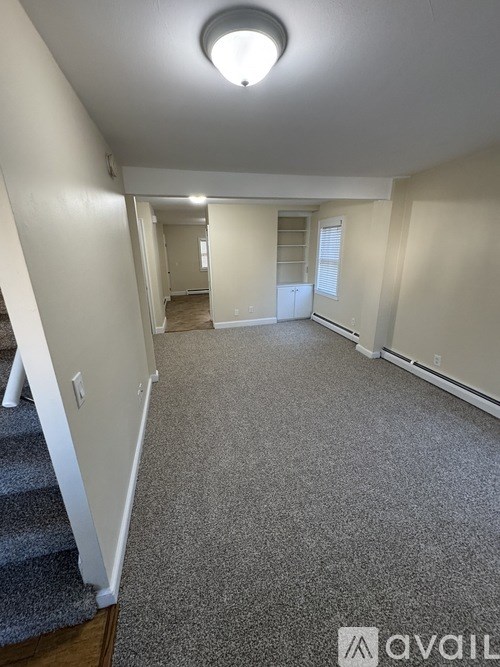 A spacious empty room with a carpeted floor and a staircase on the left side.