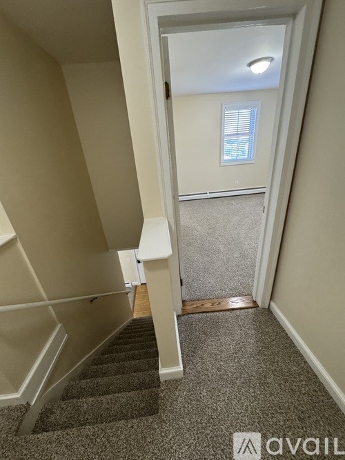A hallway with a staircase leading to a door with a window.