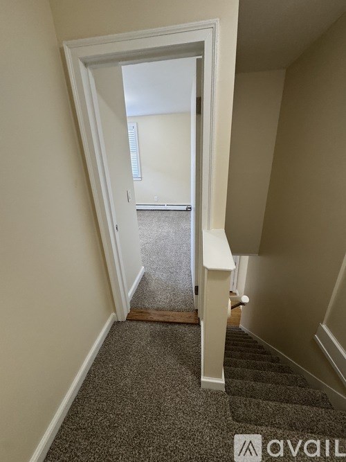 A hallway with a carpeted floor and a staircase leading to another room.