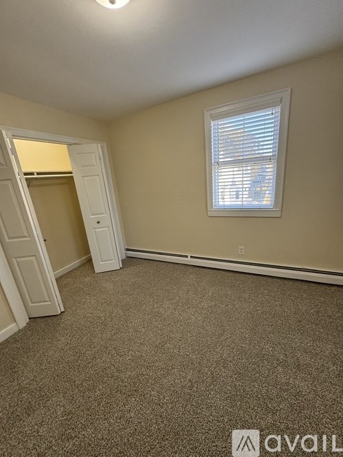 A room with a carpeted floor, a window with blinds, and a door that is open.