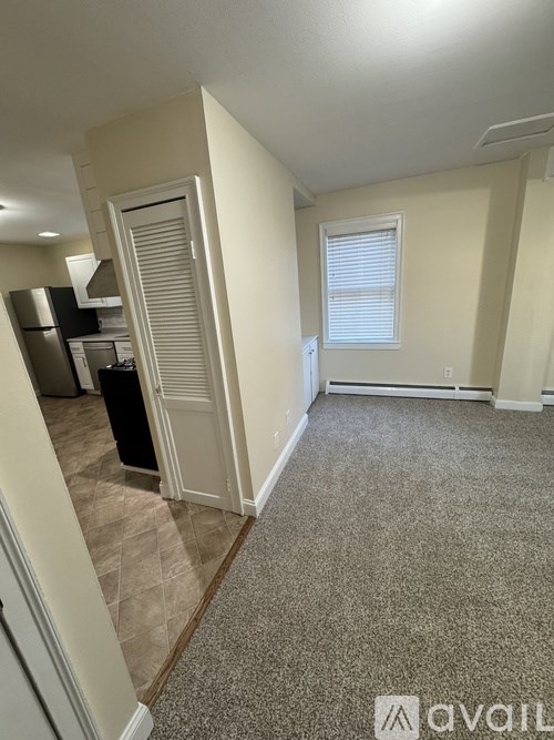 A carpeted room with a door leading to a kitchen.