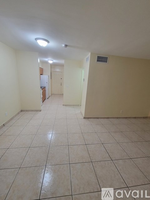 A spacious room with tiled flooring and a refrigerator in the corner.