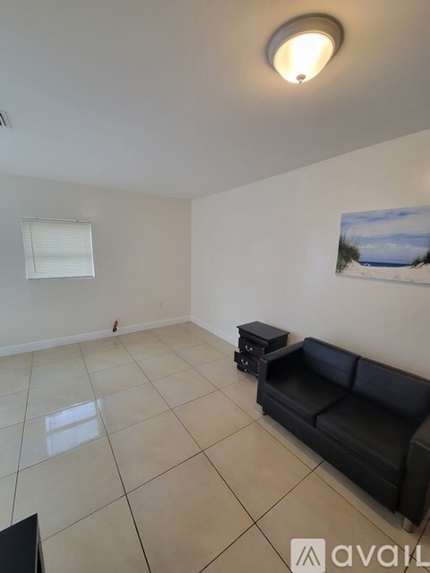 A living room with a black couch and a painting on the wall.