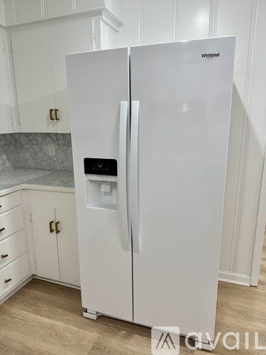A white Whirlpool refrigerator with a water and ice dispenser in the middle of the door stands in a kitchen.