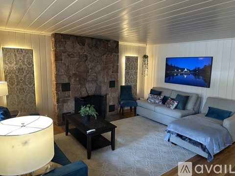 A living room with a stone fireplace and a television on the wall.