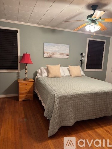 A bedroom with a bed, a nightstand with a lamp, and a ceiling fan.