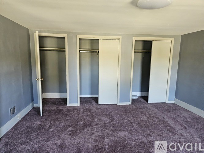 A room with grey walls and a purple carpet with four white doors.
