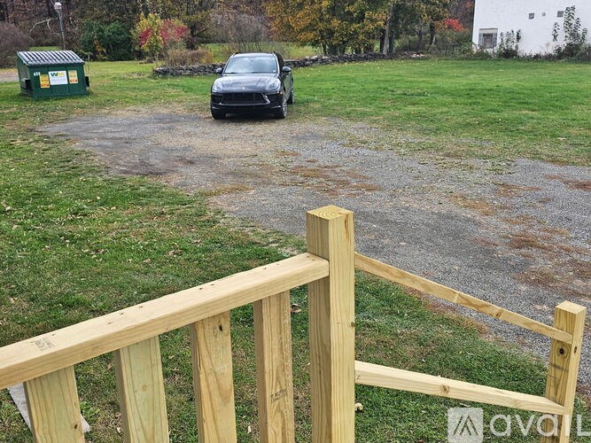 A black car is parked on a gravel driveway behind a wooden fence.