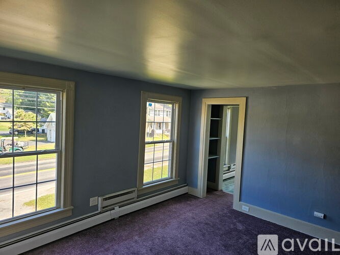 A room with purple carpet and a window overlooking a street.
