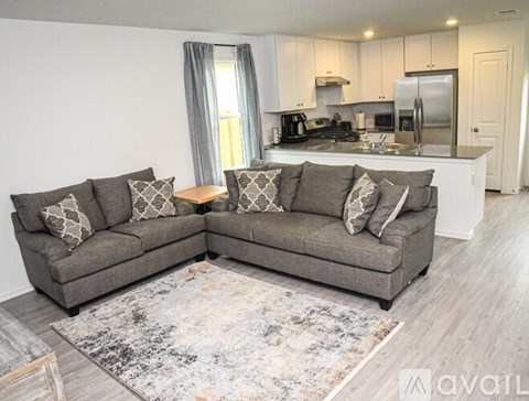 A grey couch with pillows is in the foreground of a kitchen and living room.