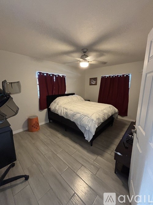 A bedroom with a bed, a ceiling fan, and a window with red curtains.