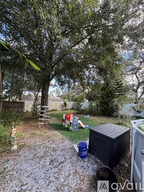 A backyard with a tree, a ladder, a cooler, and a trash can.
