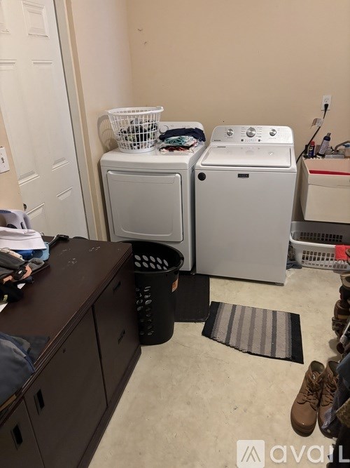 A room with a washer and dryer, a black trash can, and a brown cabinet.