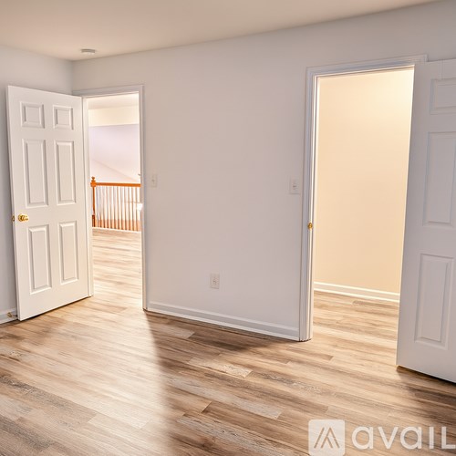 A room with white walls and wooden flooring, with two doors open.