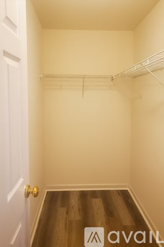 A white door is on the left of a room with a wooden floor and a white wall.