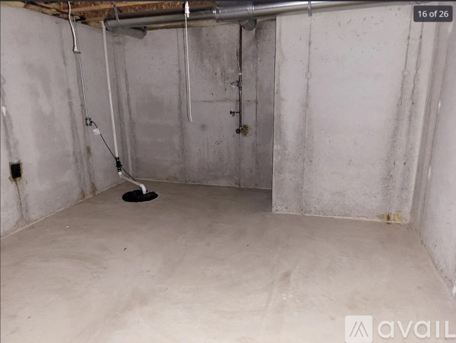 A dirty basement with a drain and pipes.