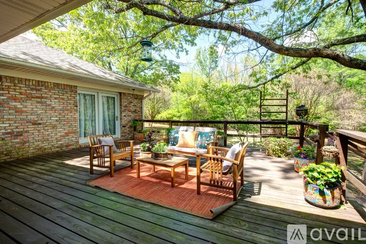 A wooden deck with chairs and a table is surrounded by greenery.