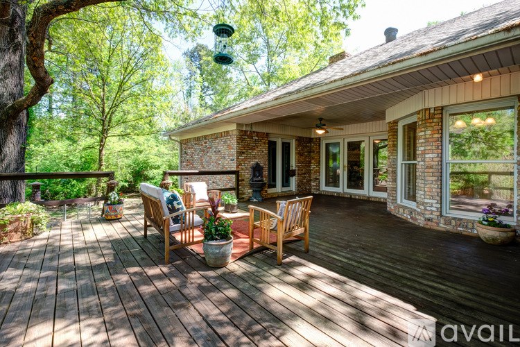 A wooden deck with chairs and a table is surrounded by greenery.
