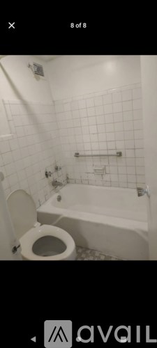 A white tiled bathroom with a toilet and bathtub.