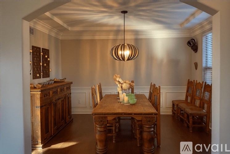 A wooden dining table with chairs and a chandelier hangs in a room with a wooden cabinet and a window.