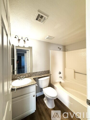 A white toilet sits in a bathroom next to a sink and a bathtub.