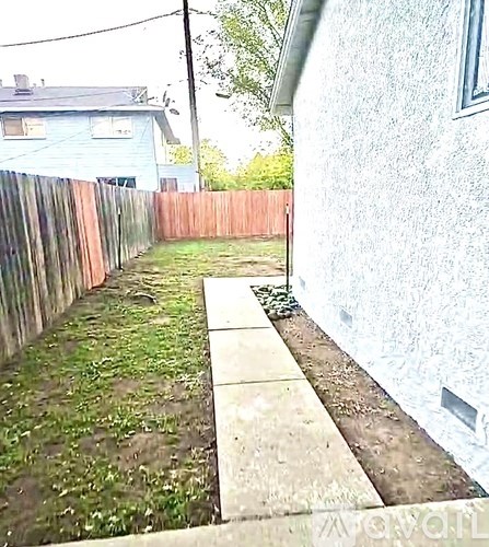 A concrete walkway leads to a grassy area in a backyard.