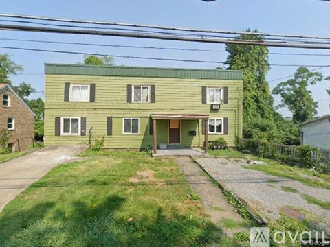 A green two-story house with a front yard and a driveway.