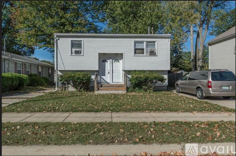 A house with a grey exterior and a white door is surrounded by a grassy area with fallen leaves.