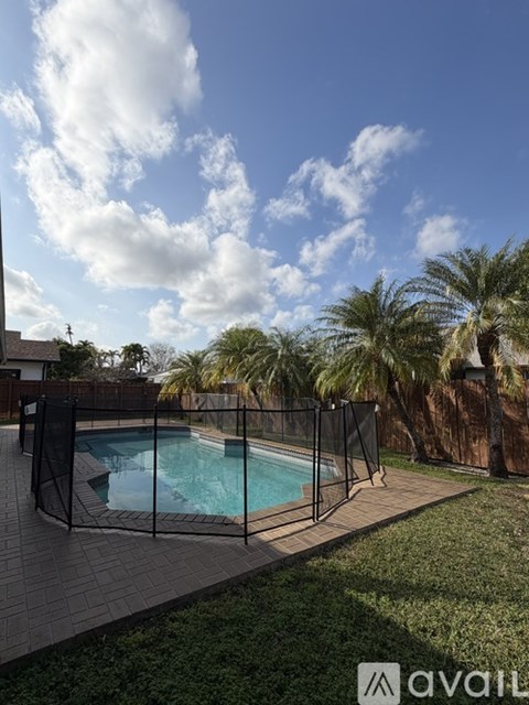 A pool surrounded by a black fence and palm trees.