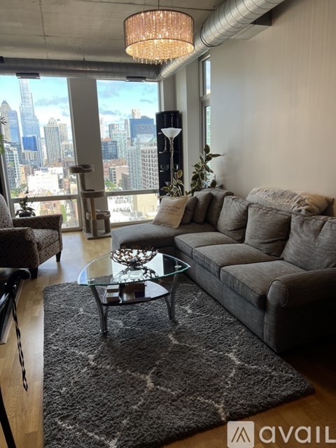 A living room with a grey couch and a glass coffee table in front of a large window.