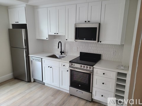 A kitchen with white cabinets and a black microwave above the stove.