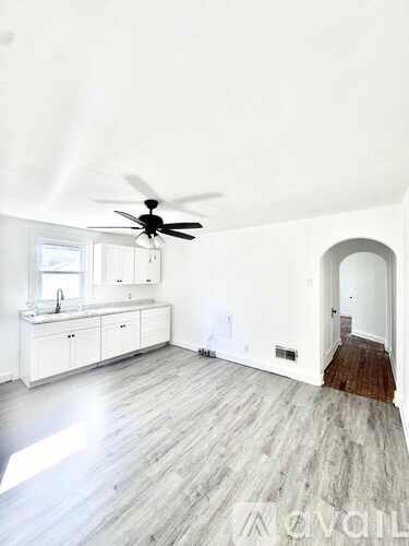 A spacious room with a ceiling fan and a kitchen area with white cabinets.