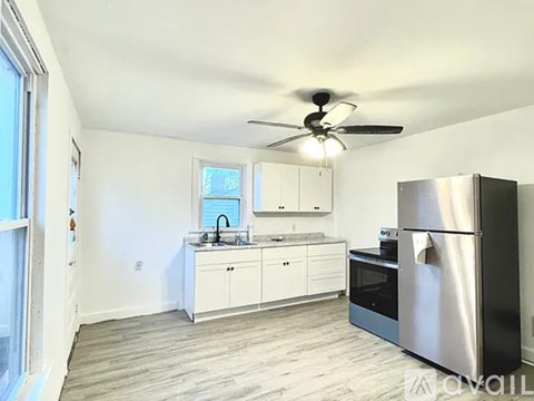 A spacious room with a ceiling fan and a kitchen area with white cabinets.