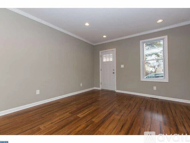A room with wooden flooring and a window showing trees outside.