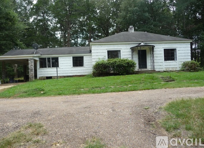 A white house with a black roof and a dirt road in front.