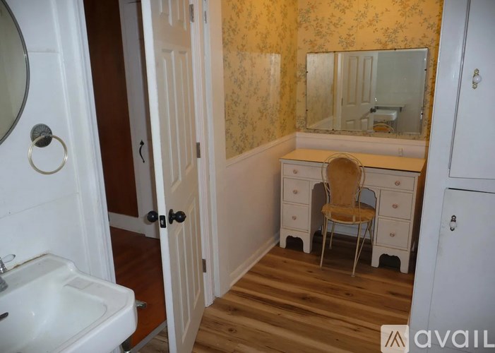 A small bathroom with a sink, mirror, and chair.