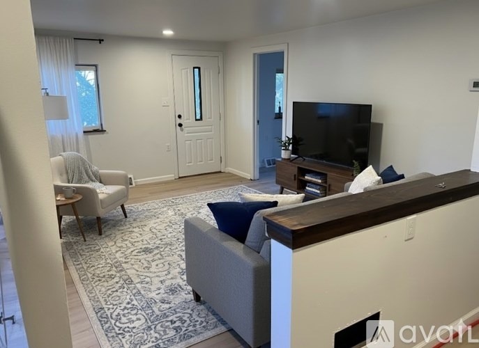 A living room with a grey couch, a white chair, a wooden entertainment center, and a rug.
