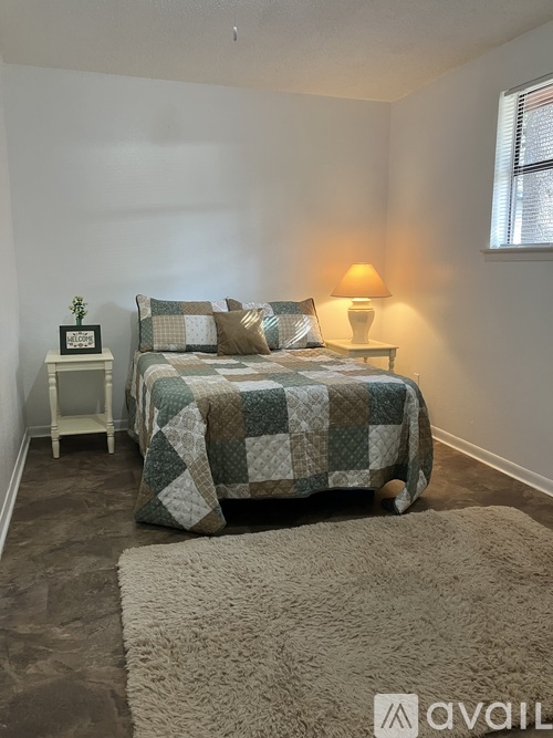 A bedroom with a bed, lamp, and a small table with a plant on it.