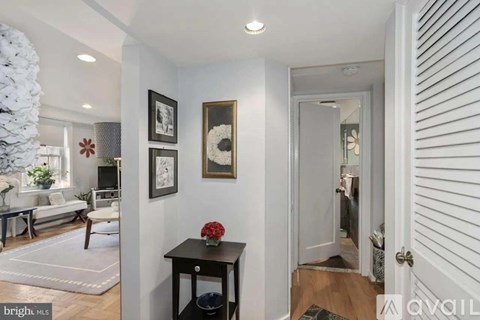 A bright living room with a white Christmas tree and a black table with a red flower on it.