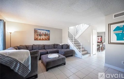 A living room with a grey couch and a painting of a group of people on the wall.