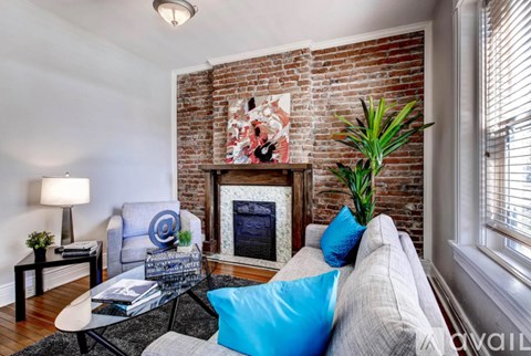 A living room with a grey couch, a fireplace, and a painting on the wall.