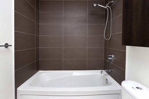 A white bathtub is in a bathroom with brown tiles.