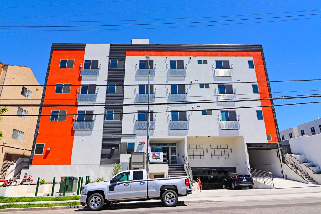 A modern building with a white and orange facade has a silver truck parked in front of it.