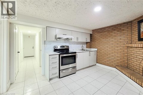 A kitchen with white cabinets and appliances, a white tile floor, and a brick wall.