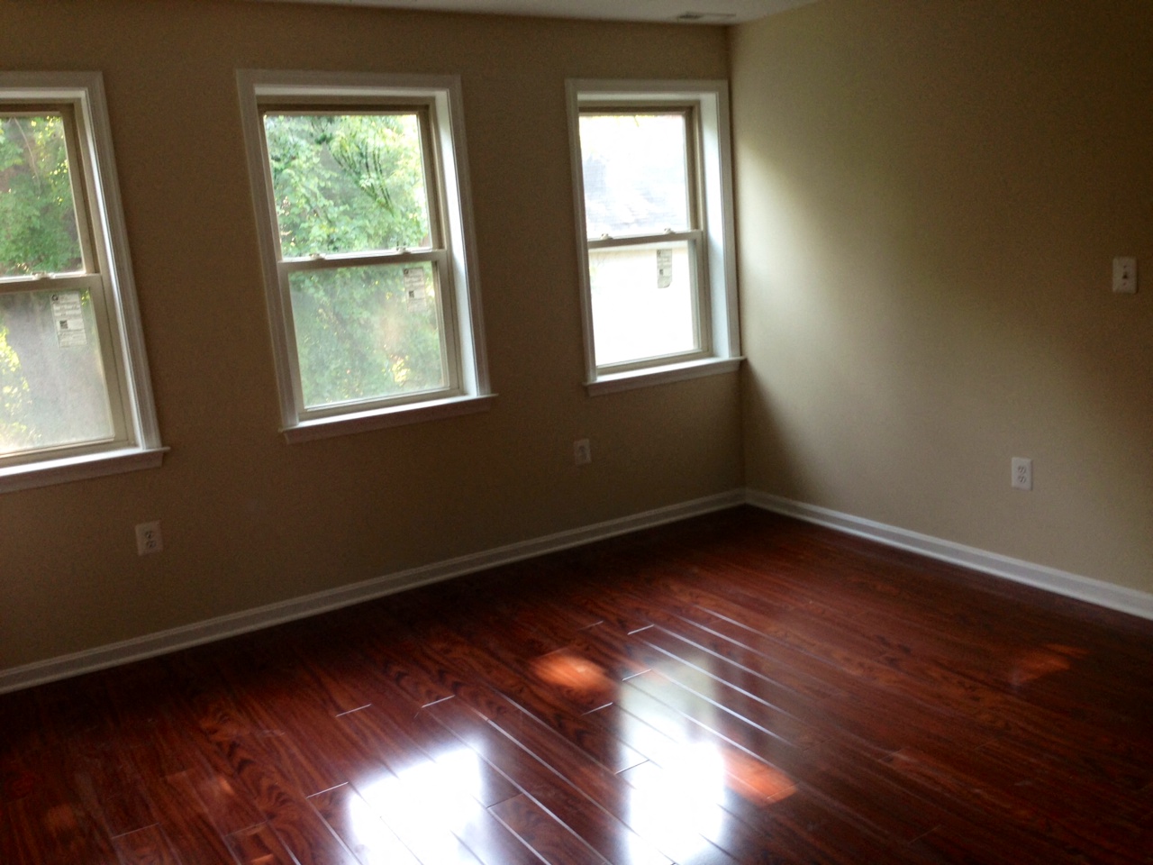 an empty room with wooden floors and three windows